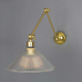Rebell Prismatic Adjustable Wall Light with prismatic glass shade and antique brass finish mounted on gray wall