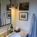 Kent Adjustable Wall Light mounted above framed artwork in cozy modern bathroom with marble countertop and brass faucet