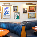 Dublin Picture Light illuminating framed artwork in a modern dining space with blue leather seating and wooden tables