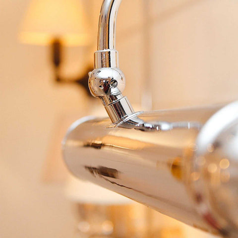 Close-up of polished chrome Dulwich Picture Light with adjustable arm and sleek lamp holder attached to a wall-mounted fixture, designed for illuminating artwork with elegant lighting.
