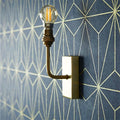 Pooky Melville vintage glass wall light with antique brass finish mounted on geometric patterned wall