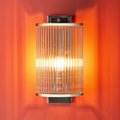 Pooky Roddy Wall Light with clear glass rods in brushed nickel finish on orange wall providing warm ambient lighting