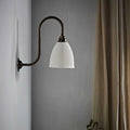 Hartlip small ribbed ceramic shade wall light with bronze curved arm mounted on gray wall next to beige curtains