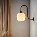 Stanford medium ceramic shade wall light with matte finish and warm glow mounted on curved bronze arm