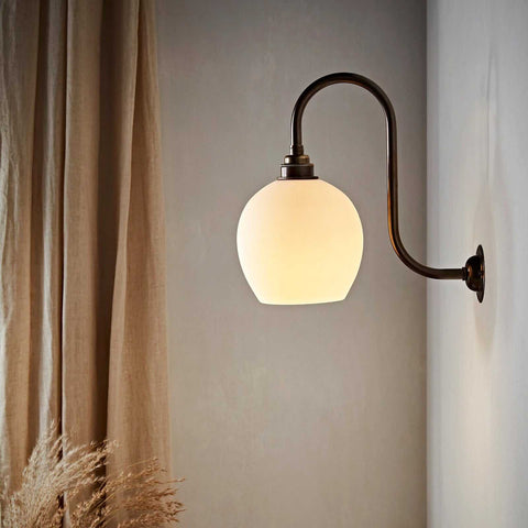 Stanford Medium Ceramic Shade wall light with matte finish and warm glow mounted on bronze curved arm against neutral wall and curtains