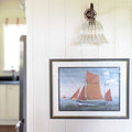 Bodium Small Ribbed glass shade wall light with antique brass finish above framed sailboat artwork in a modern interior.