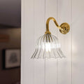Bodium small ribbed glass shade wall light with antique brass curved arm mounted on white wooden wall