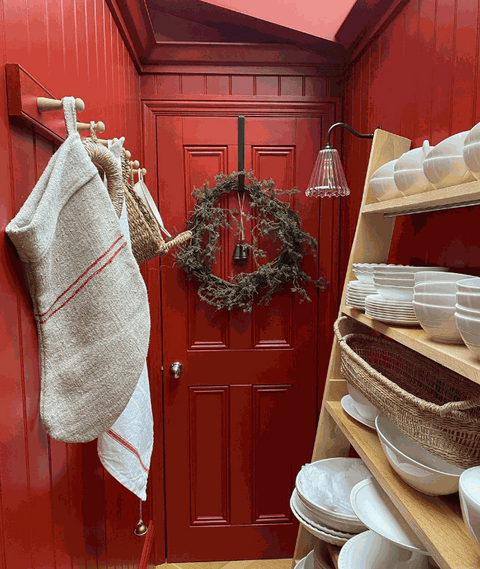 Rye Ribbed Glass Small Wall Light with ribbed glass shade and warm ambient glow mounted on red wall in cozy hallway with shelves and hanging towels.