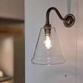 Rye Small Clear Glass Shade wall light with metal arm and exposed bulb mounted on white wall
