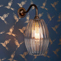 Camber Medium Ribbed Glass wall light with fluted glass shade and bronze finish mounted on bird-patterned blue wallpaper background