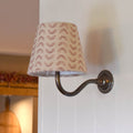 Pink Sycamore Linen fabric shade wall light with curved metal arm mounted on white wall providing warm ambient lighting