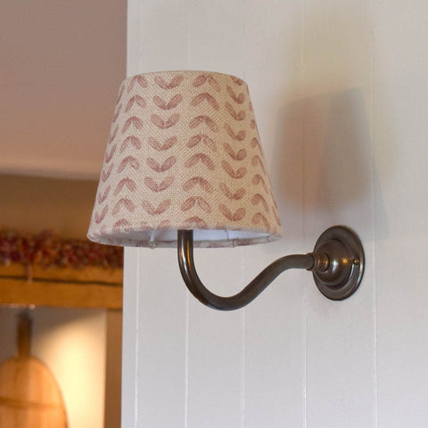 Pink Sycamore Linen fabric shade wall light with bronze curved arm mounted on white wall providing warm ambient glow