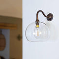 Soho Medium Clear Glass Shade wall light with antique brass finish and hand-blown glass globe mounted on white wall