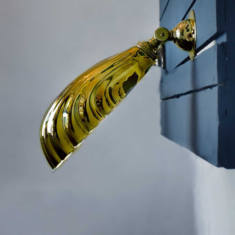 Hadlow adjustable vintage brass shell wall light with Art Deco design mounted on dark blue wall