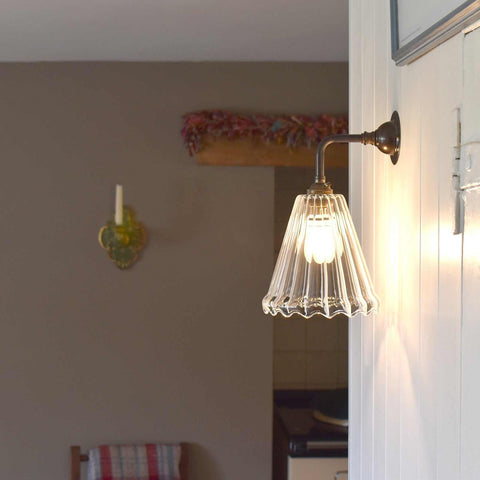Rye Ribbed Glass small wall light with ribbed glass shade and curved base mounted on a white wall emitting soft warm light