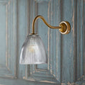 Pooky Tiny Qilin bathroom wall light with swan neck brass arm and prismatic glass shade on textured blue wall