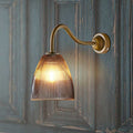 Pooky Tiny Qilin bathroom wall light with swan neck brass arm and prismatic glass shade illuminating softly on textured wall