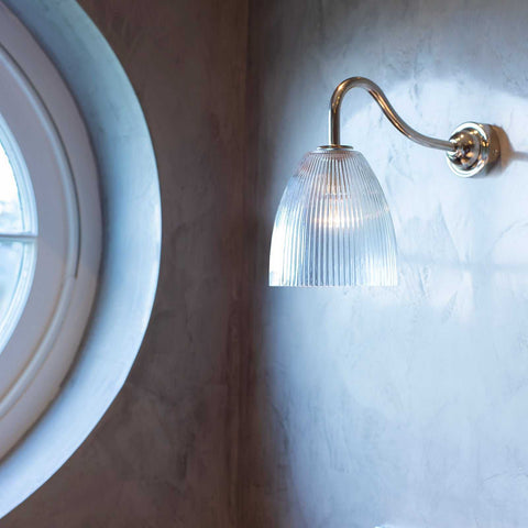 Pooky Tiny Qilin bathroom wall light with swan neck and prismatic glass shade mounted on grey wall near circular window