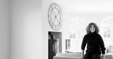 Hilary the founder of the company sitting on the sofa of a modern house with a large clock and fire place