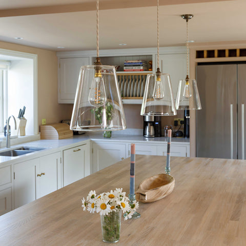 Newbury large clear glass shade pendant lights hanging over a kitchen island with white cabinetry and wooden countertop
