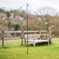 Sturdy steel festoon pole supporting outdoor string lights in garden with wooden bench and fence background