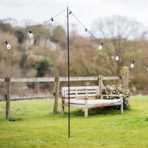 Sturdy steel festoon pole supporting outdoor string lights in garden with wooden bench and fence background
