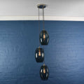 Camber Large Smoked Glass cluster pendant light with three oval smoked glass shades hanging against a blue brick wall