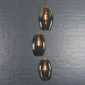 Camber Large Smoked Glass cluster pendant light with three oval smoky glass shades and exposed filament bulbs hanging against a gray brick wall