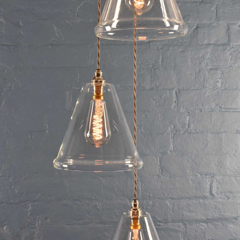 Rye medium clear glass shade cluster pendant light with hand-blown glass and adjustable cords against a gray brick wall background