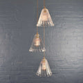 Rye medium ribbed glass shade cluster pendant light with three hand-blown glass shades hanging against a gray brick wall