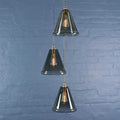 Rye medium smoked glass shade cluster pendant light with three hand-blown smoked glass shades and exposed filament bulbs against a blue brick wall background