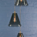 Rye medium smoked glass shade cluster pendant light with hand-blown glass and adjustable metal fixtures against a blue brick wall