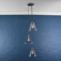 Rye medium clear glass shade cluster pendant light with three hand-blown glass shades and adjustable hanging cords against a blue brick wall background
