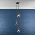 Modern Rye small clear glass shade cluster pendant light with three adjustable hanging clear glass shades over blue brick wall background