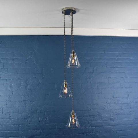Rye small clear glass shade cluster pendant light with adjustable hanging lengths and exposed bulbs against a blue brick wall