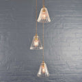 Rye small ribbed glass shade cluster pendant light with three hand-blown glass shades and adjustable flex cables against a gray brick wall background