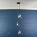 Rye Small Ribbed Glass Shade cluster pendant light with three clear ribbed glass shades hanging at varying lengths against a blue wall