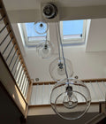 A modern multi-light pendant chandelier with four clear glass globe shades of varying sizes and black metal hardware, hanging from the ceiling of a bright home with skylights and a wooden staircase railing.
