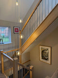 A modern wooden staircase with light oak rails and balusters, featuring a hanging glass globe pendant light and framed wall art in a residential interior.