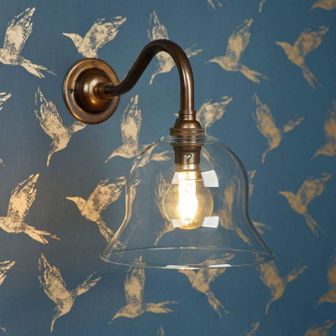 Bodium Small wall light with clear glass shade and antique brass arm on blue bird patterned wall